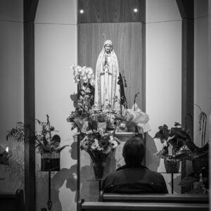 grayscale photography of person sitting in front of religious figure